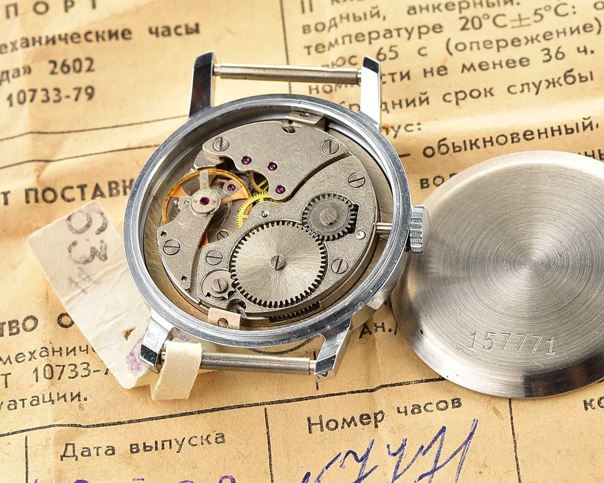 Pobeda-10448_KOM_1963 Mechanical wristwatch POBEDA with open case back, showing gears and movement, placed on vintage paperwork.