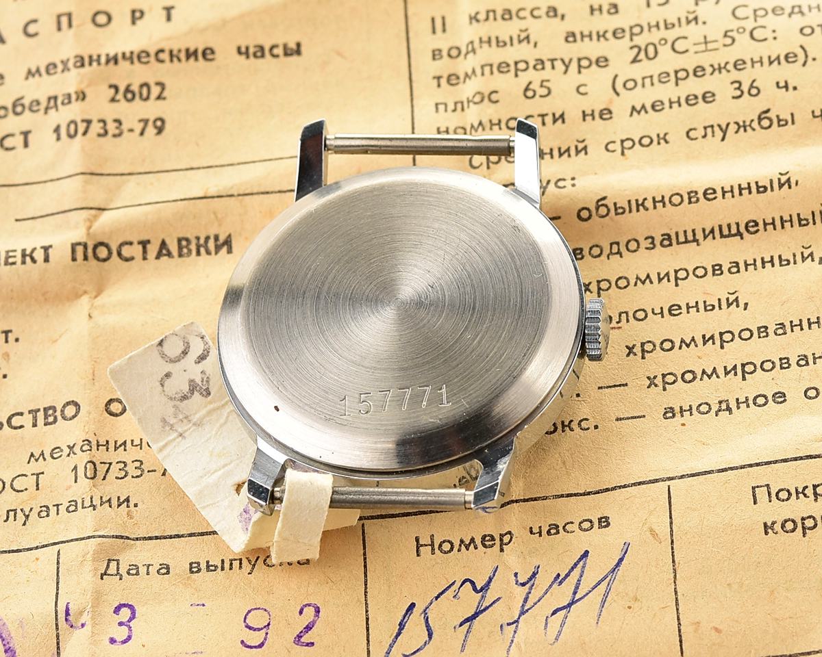 Back view of a Pobeda mechanical wristwatch on vintage papers, highlighting stainless steel case.